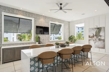 Apartment clubhouse with large kitchen island, bar stools, wall-mounted TV, and windows.