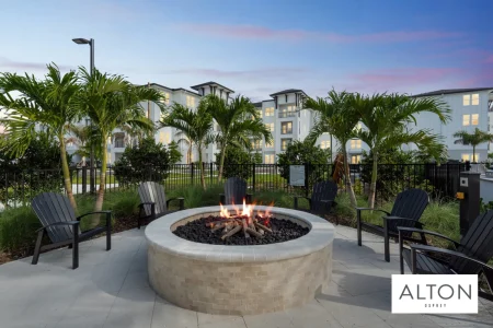 Outdoor fire pit with chairs, palm trees, and apartment buildings in the background.