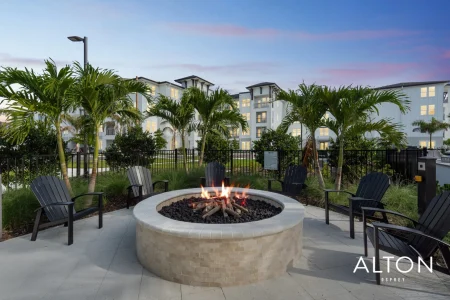 Outdoor fire pit with chairs, palm trees, and apartment buildings in the background.