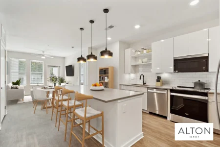Modern apartment kitchen with island, bar stools, white cabinets, and stainless steel appliances.