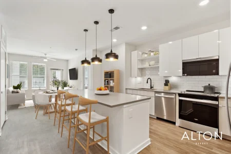 Modern apartment kitchen with island, bar stools, white cabinets, and stainless steel appliances.