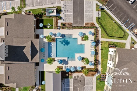 Aerial view of community pool with umbrellas and surrounding buildings